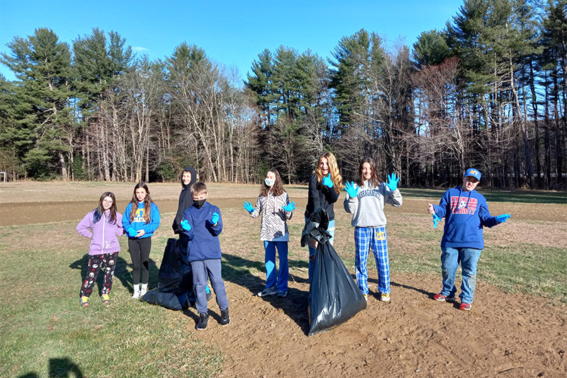 Students wearing gloves and holding giant garbage bags outside