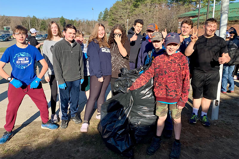 Students smiling together in front of the school with their multiple bags of collected trash for Earth Day